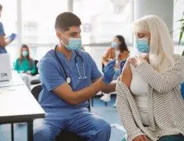 Senior Patient Getting Vaccinated Against Coronavirus Sitting In Medical Center