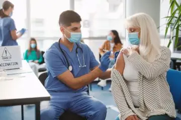 Senior Patient Getting Vaccinated Against Coronavirus Sitting In Medical Center